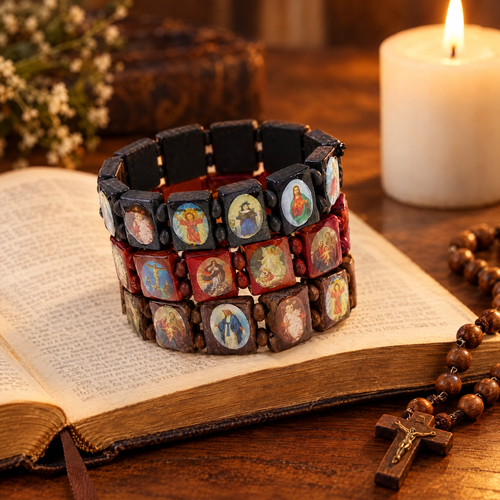 Black, red and brown wooden saints rosary bracelets on an open Bible beside a candle