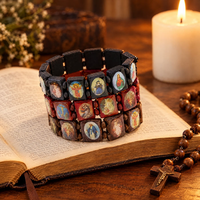 Black, red and brown wooden saints rosary bracelets on an open Bible beside a candle